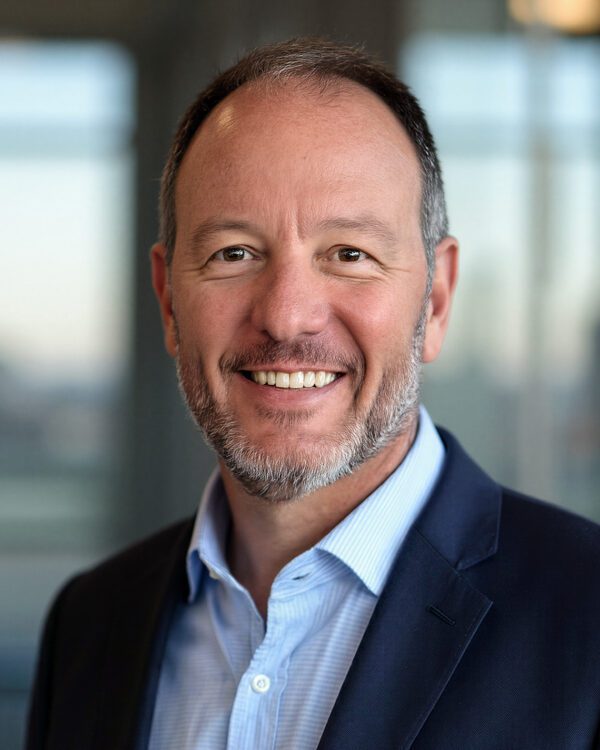 Brad Murr gentleman with a peppered beard wearing a blue dress shirt and navy suit jacket smiling inside an office setting