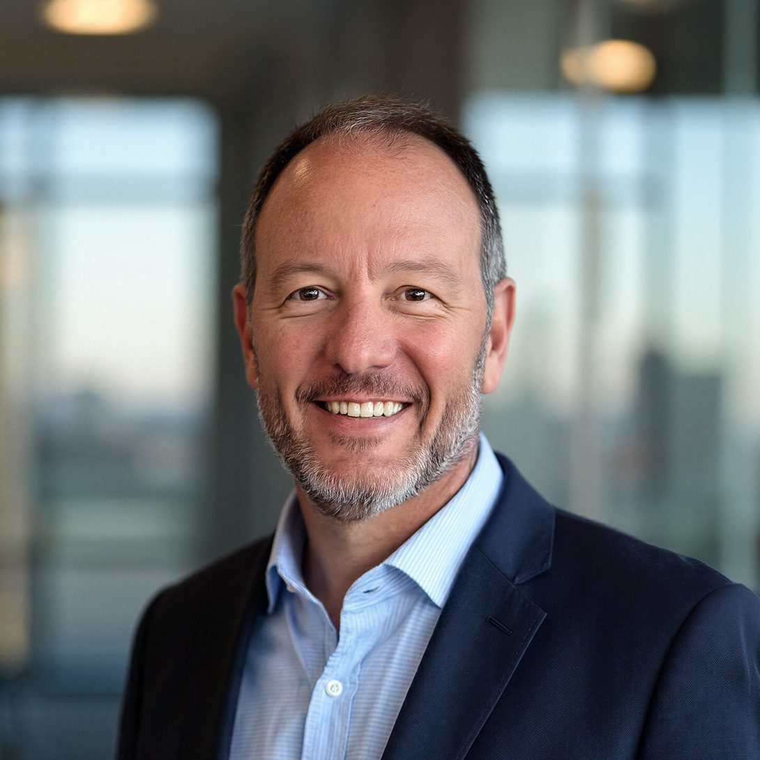 Brad Murr gentleman with a peppered beard wearing a blue dress shirt and navy suit jacket smiling inside an office setting