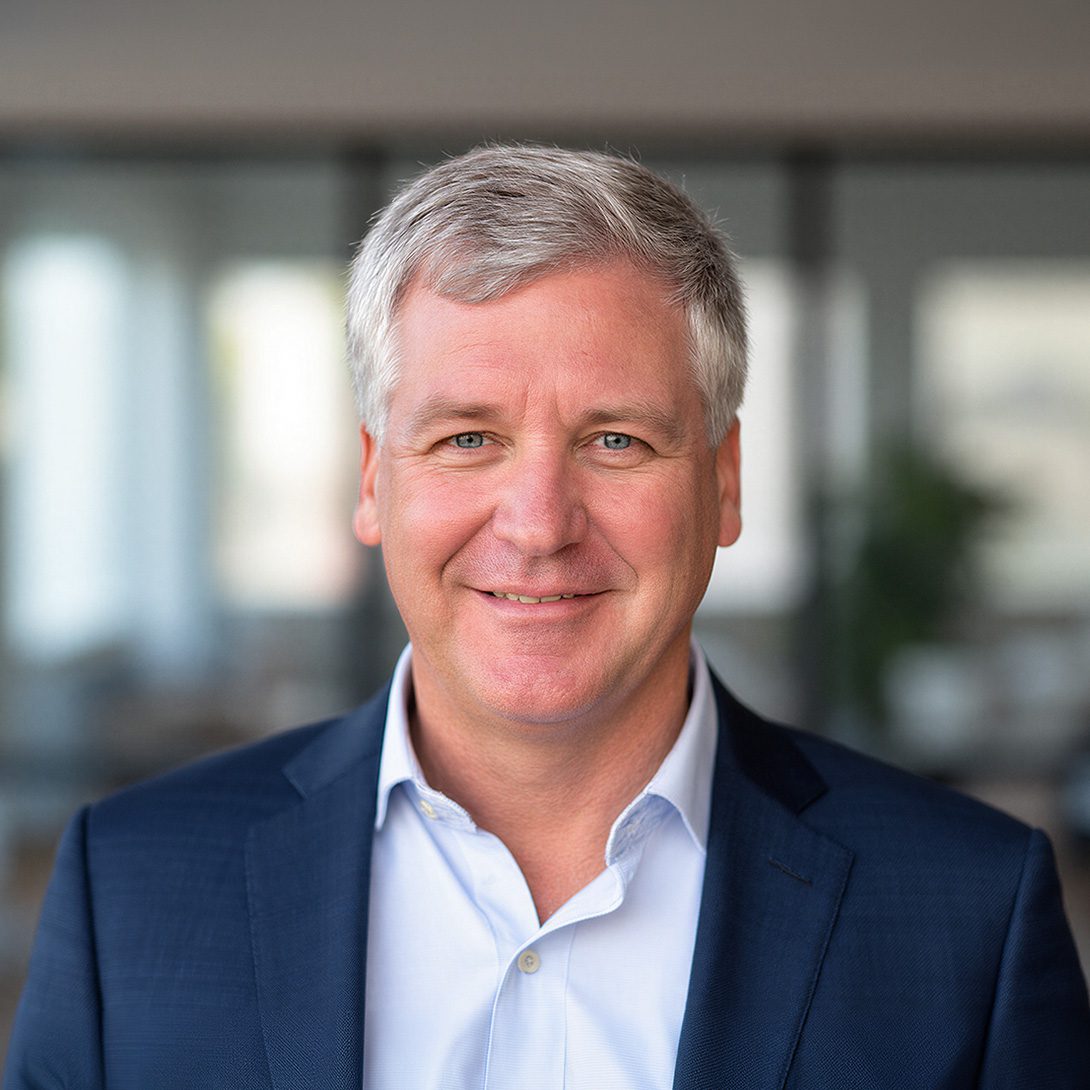 gentleman with gray hair and a sports coat smiling inside an office environment