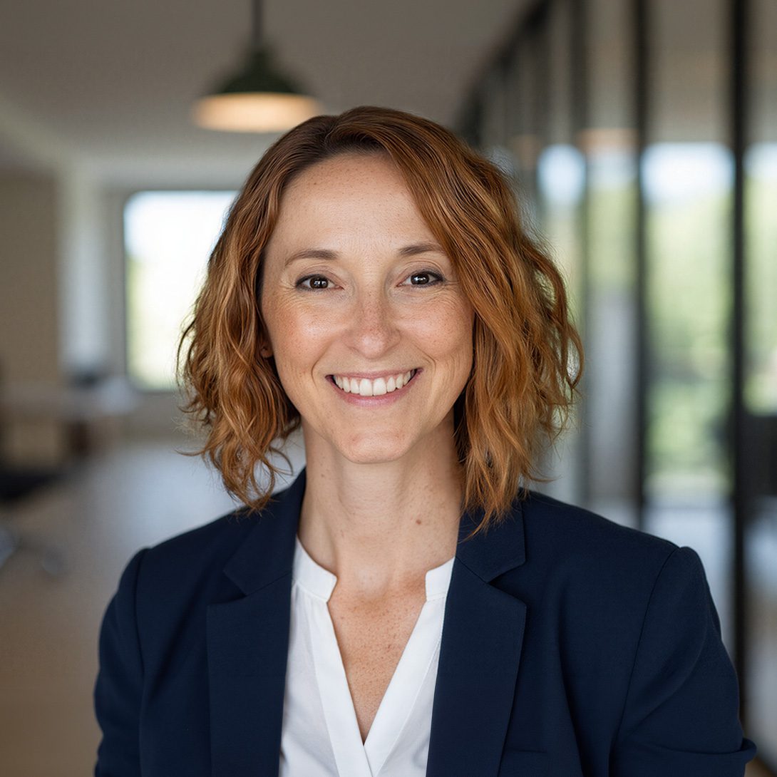 woman in business attire with red/blonde hair smiling inside an office