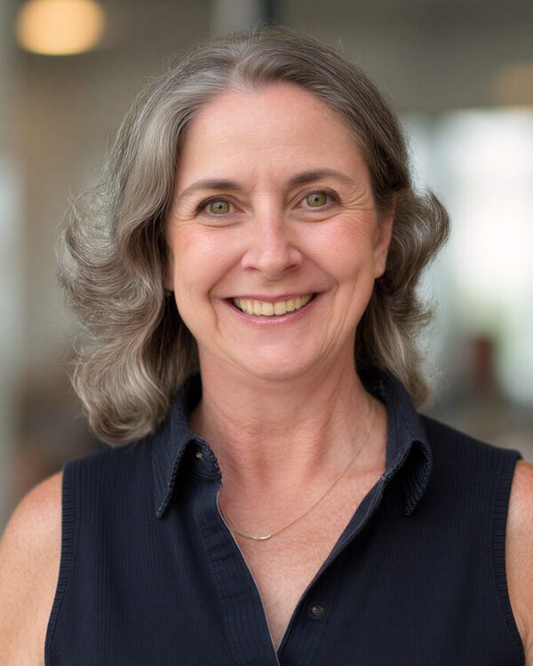 woman with gray wavy hair in a black sleeveless dress smiling inside an office building