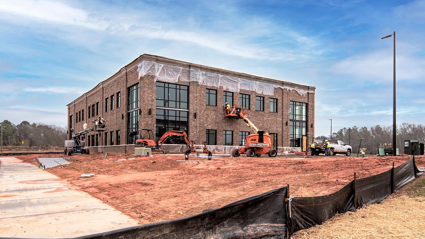 Future Atrium Health 2-story 20,000 SF medical office building under construction at The Crossing at Doby's Bridge, exterior nearly complete with red clay mud where landscaping will go