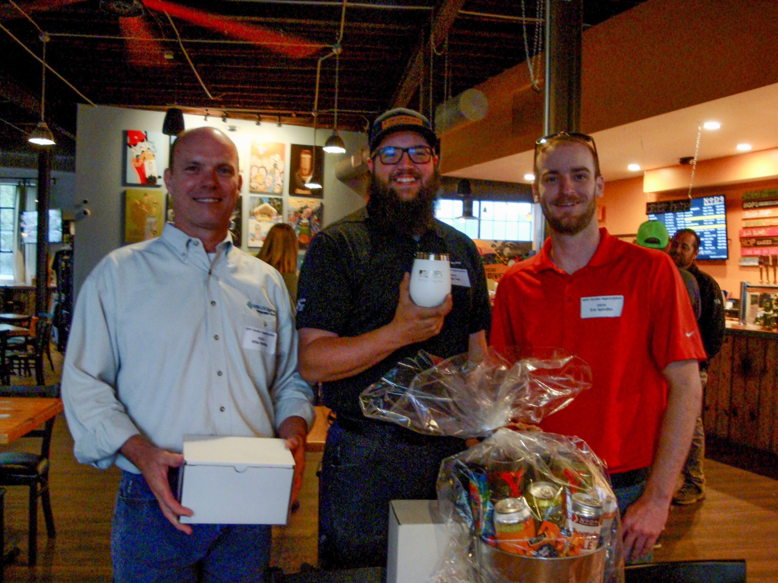 MPV event at NoDa brewery three adult men smiling in front of gift basket