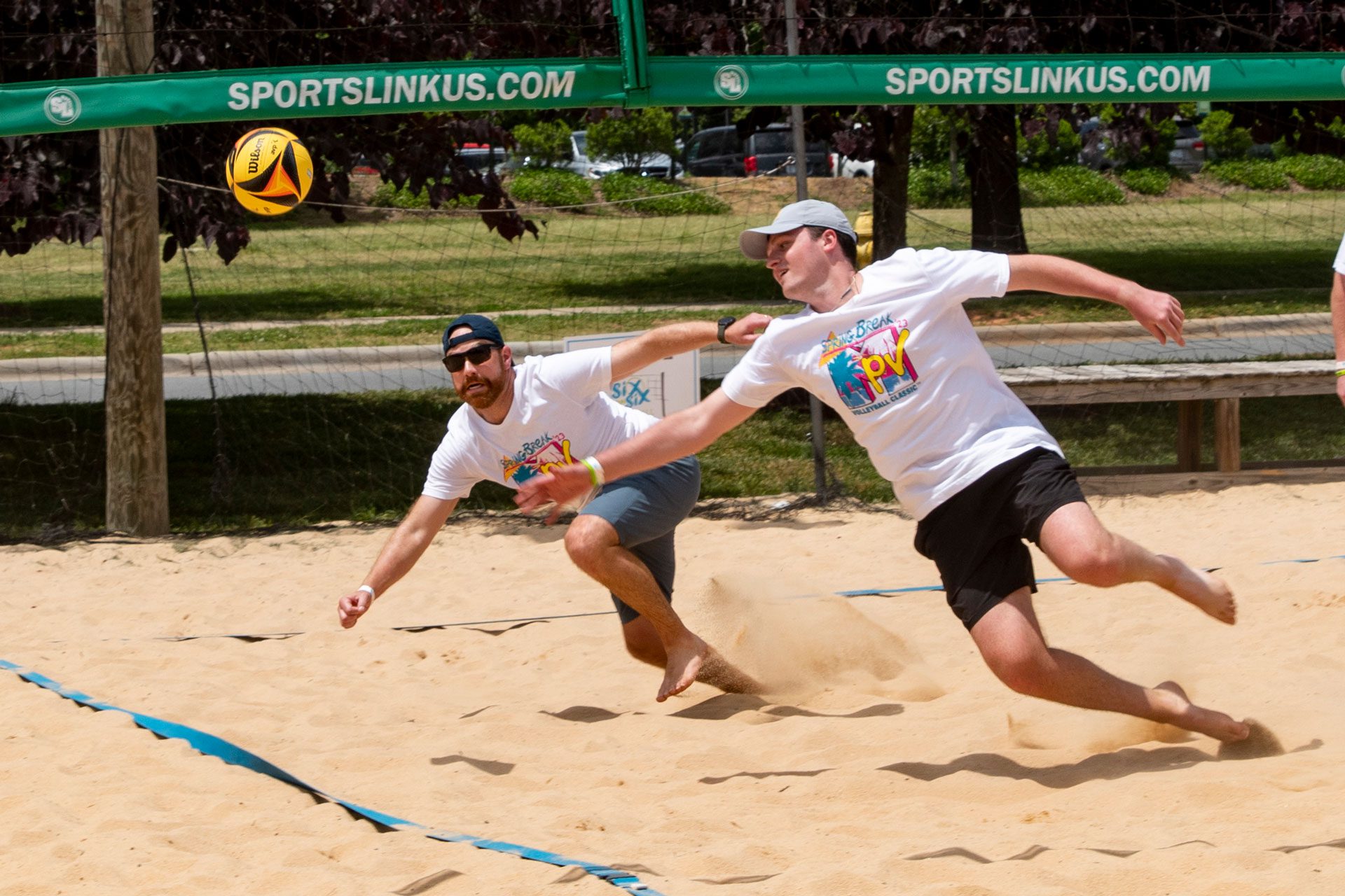 MPV volleyball action two players dive for a ball on a sand court