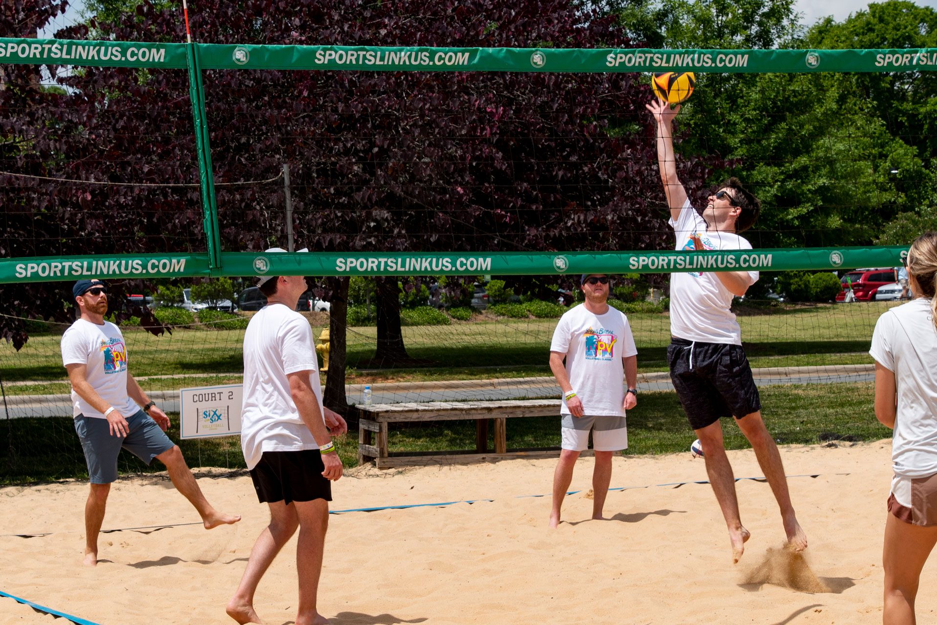 volleyball scene with one player jumping for ball on sand court and others watching