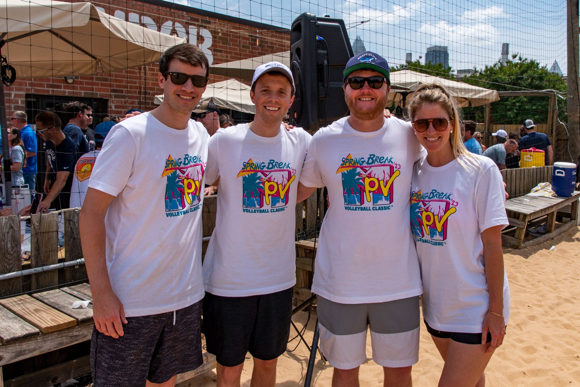 four people smiling with MPV shirts on at a volleyball tournament