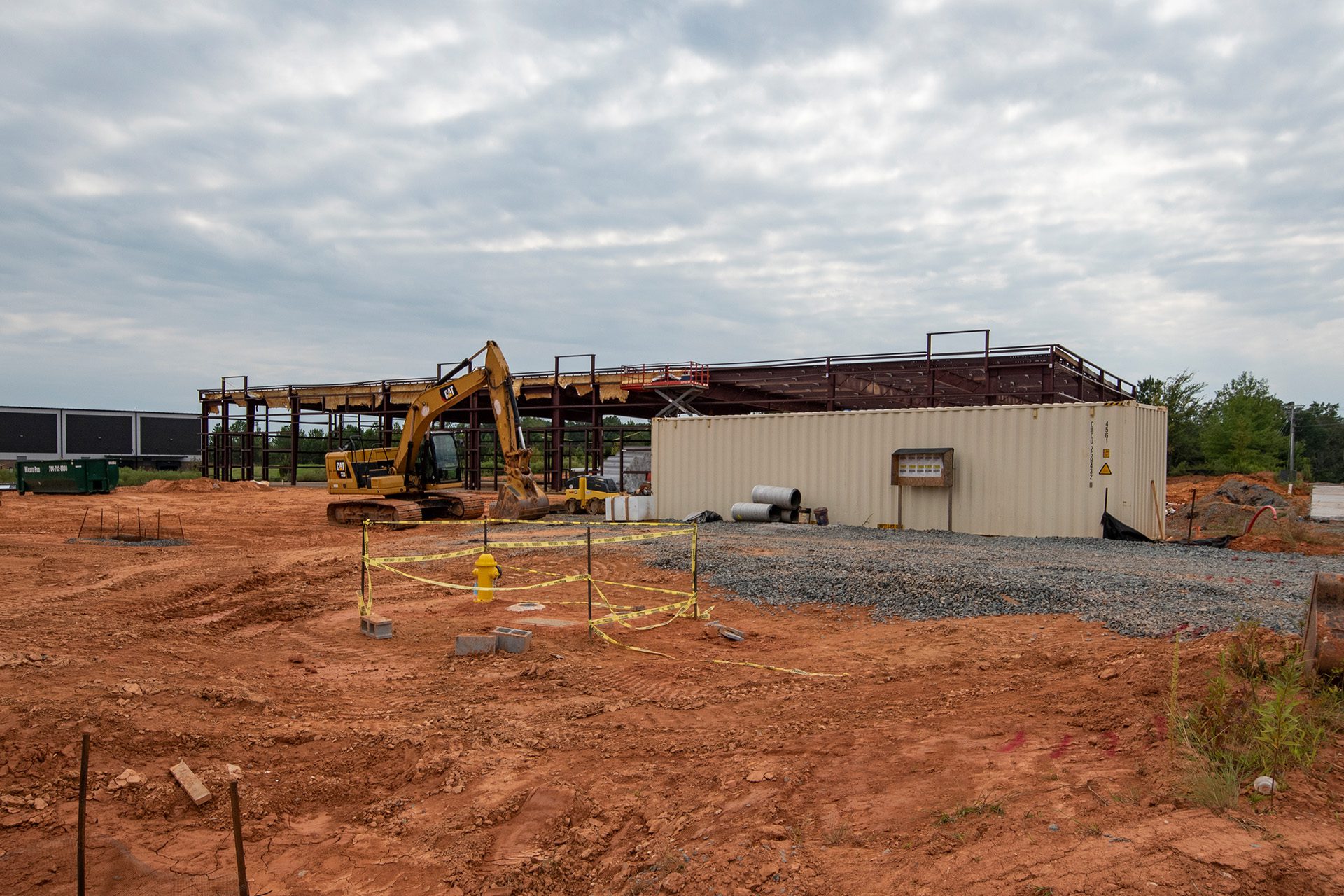flex building under construction with red dirt on ground and steel up, construction equipment and trailer