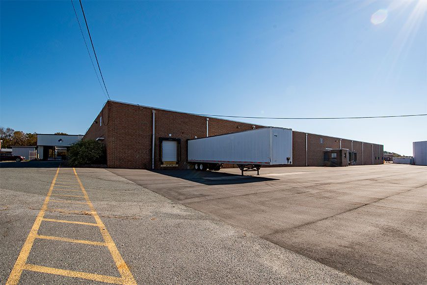exterior of brick industrial building with blue skies and parking lot