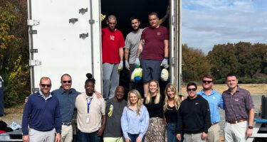 13 people standing smiling outside a semi truck after loading with food for Thanksgiving
