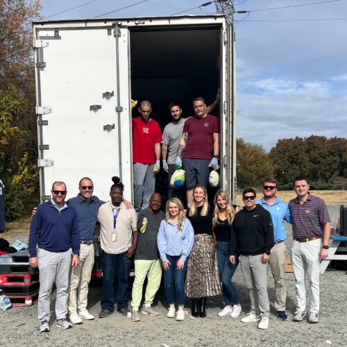 13 people standing smiling outside a semi truck after loading with food for Thanksgiving