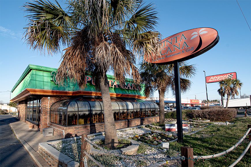 Restaurant building with green roof , palm tree and sign in front