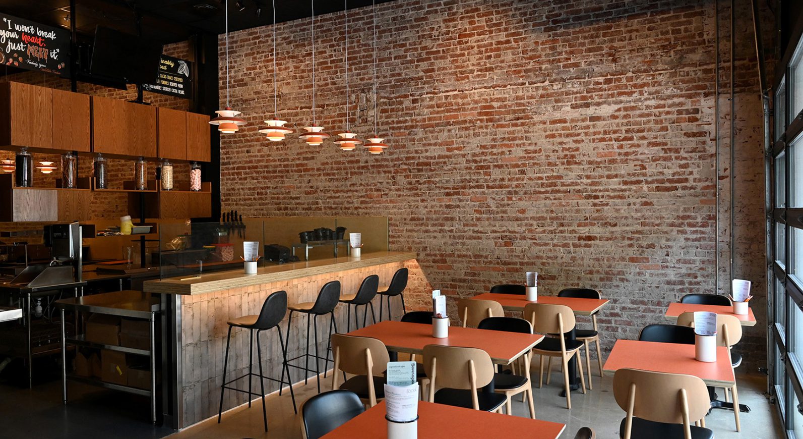Interior photo of bar seating, exposed brick, and tables with chairs