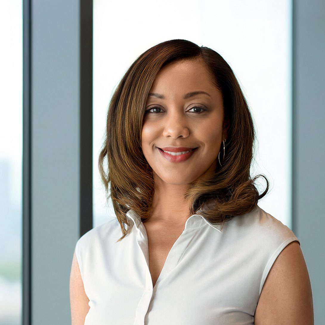 Woman in a white blouse smiling by a window inside a high rise office building