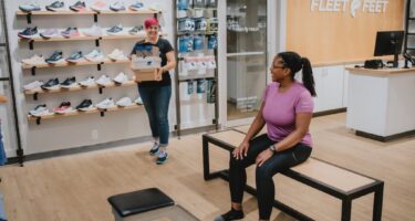 interior of Fleet Feet store with two women, one sales associate helping a seated woman find running shoes