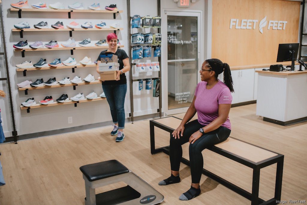 interior of Fleet Feet store with two women, one sales associate helping a seated woman find running shoes