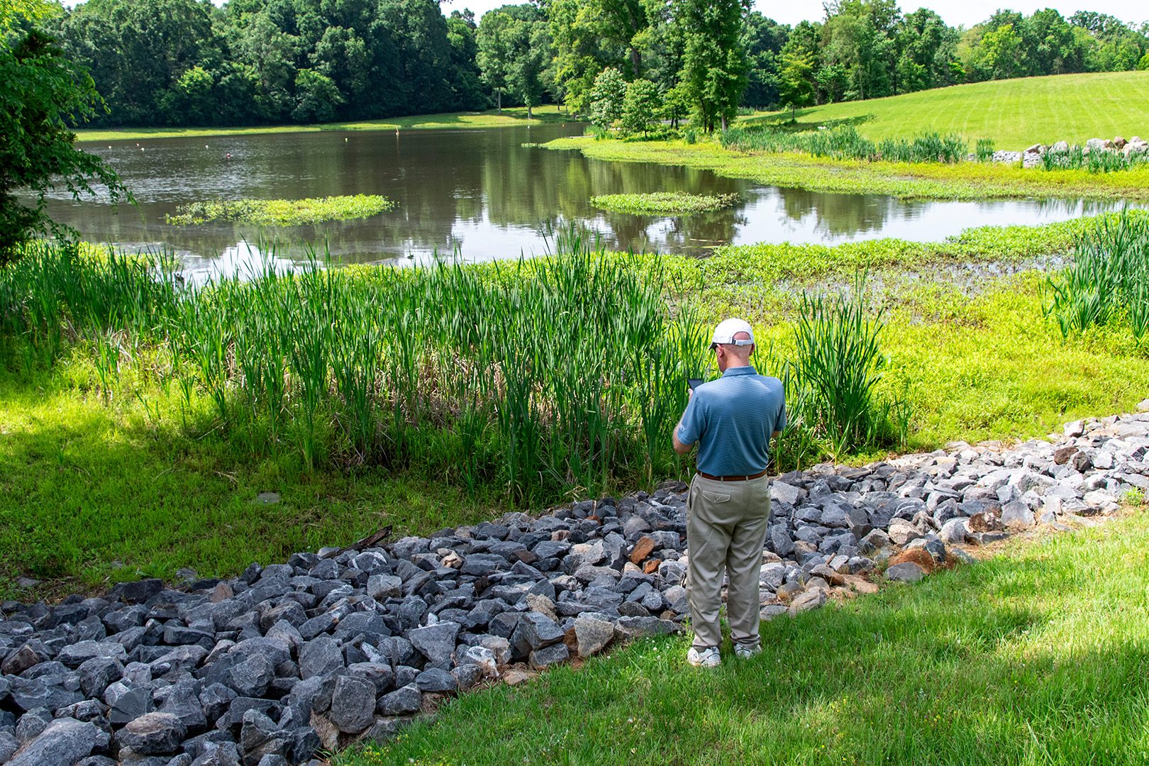 man standing in front of a stormwater pond with large rocks in foreground inspecting the SCM