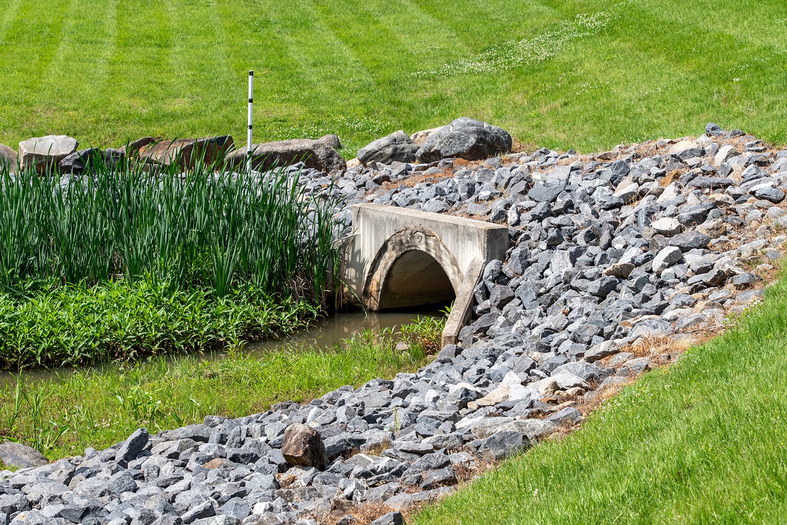 concrete orifice surrounded by rocks as part of SCM stormwater management pond