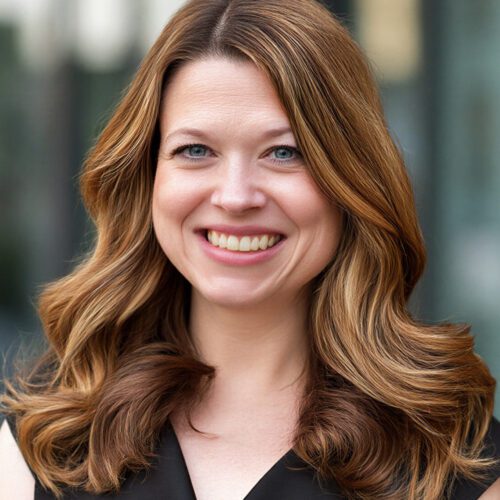 woman with brunette hair and a black blouse smiling outside office buildings