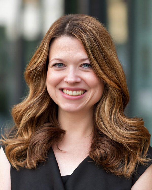 woman with brunette hair and a black blouse smiling outside office buildings