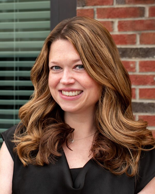 woman with brunette hair and a black blouse smiling outside a brick building