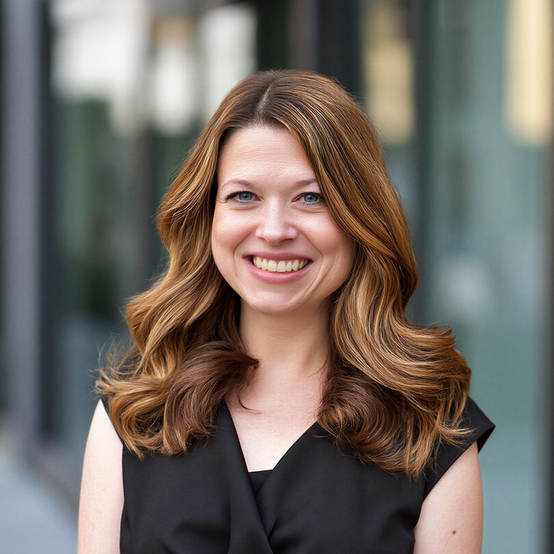 woman with brunette hair and a black blouse smiling outside office buildings