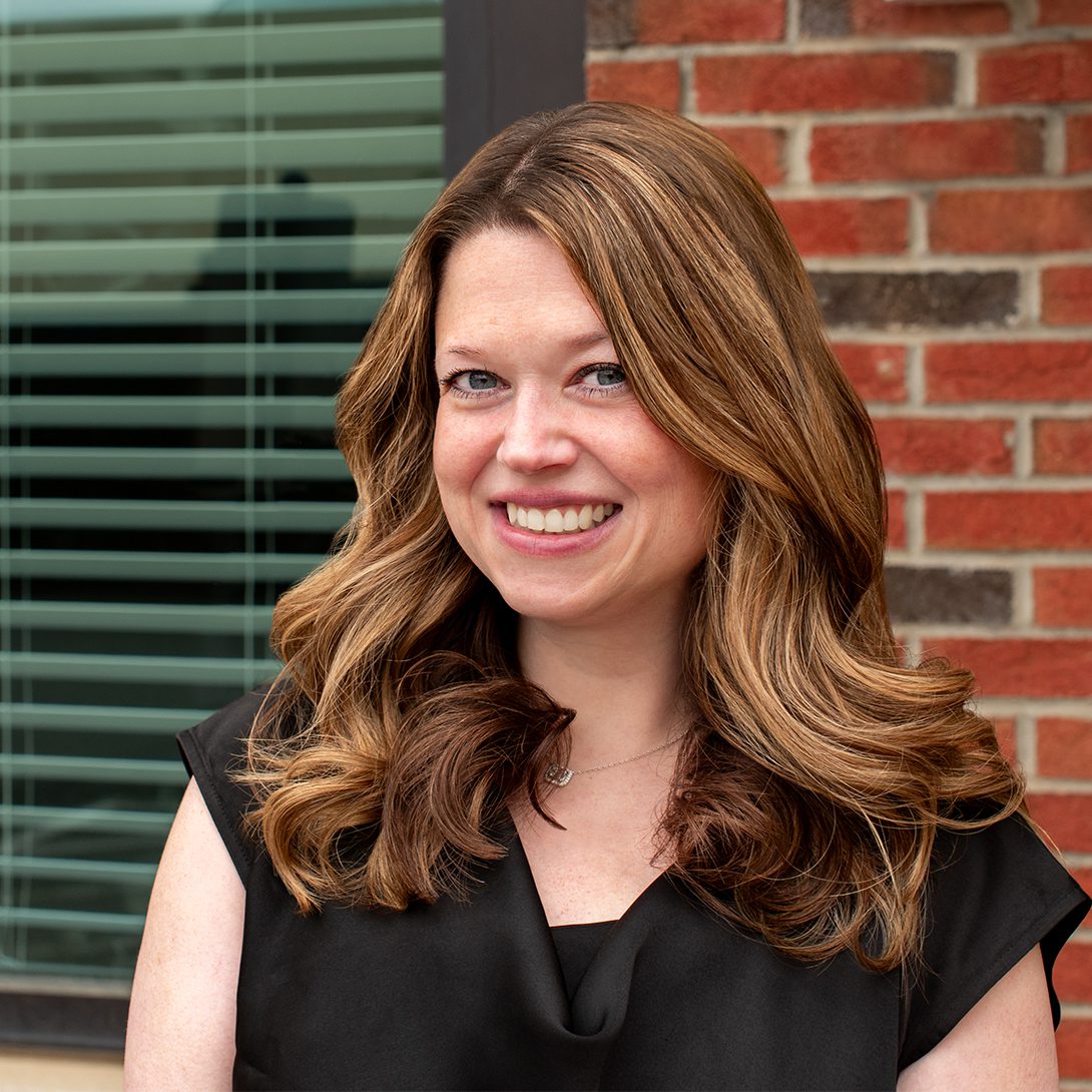 woman with brunette hair and a black blouse smiling outside a brick building