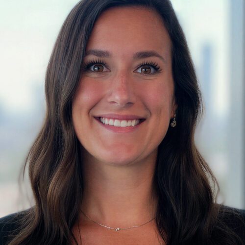 Sarah Sipe lease administrator young woman with long brown hair inside an office building in a black blazer