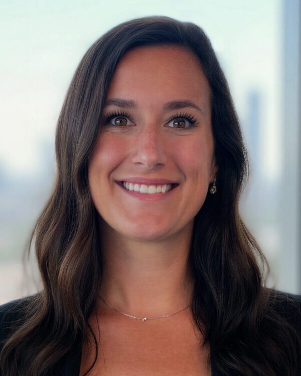 Sarah Sipe lease administrator young woman with long brown hair inside an office building in a black blazer